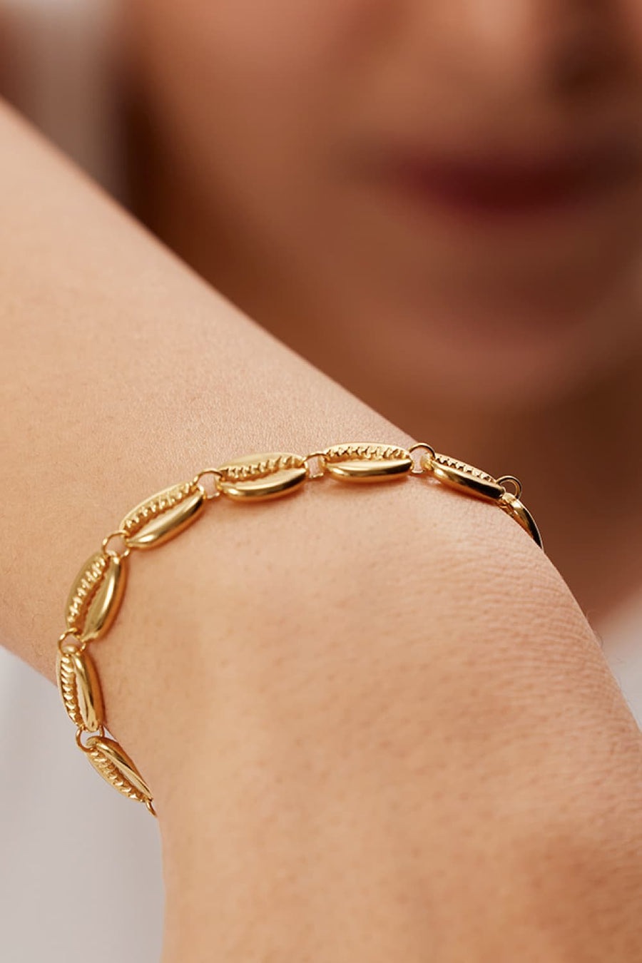 Gold cowrie shell bracelet with textured detailing on a wrist.