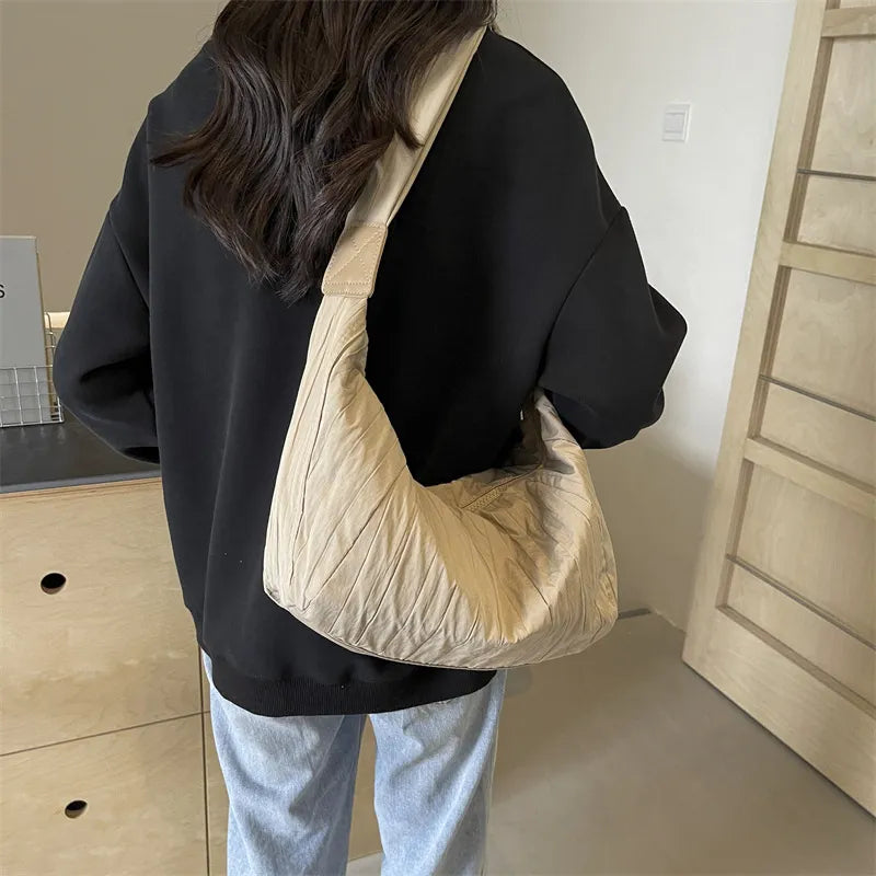 Beige quilted crescent shoulder bag with ruched detailing and a single strap.