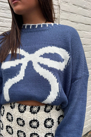Dusty blue knit crewneck sweater with a white graphic bow pattern and contrast stitching.