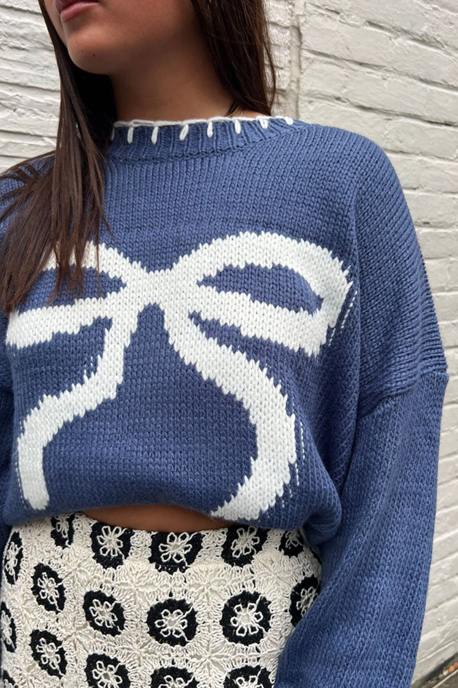 Dusty blue knit crewneck sweater with a white graphic bow pattern and contrast stitching.