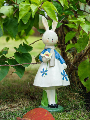 Resin floral rabbit ornament with blue flowers, holding a white flower, wearing a blue jacket and scarf.