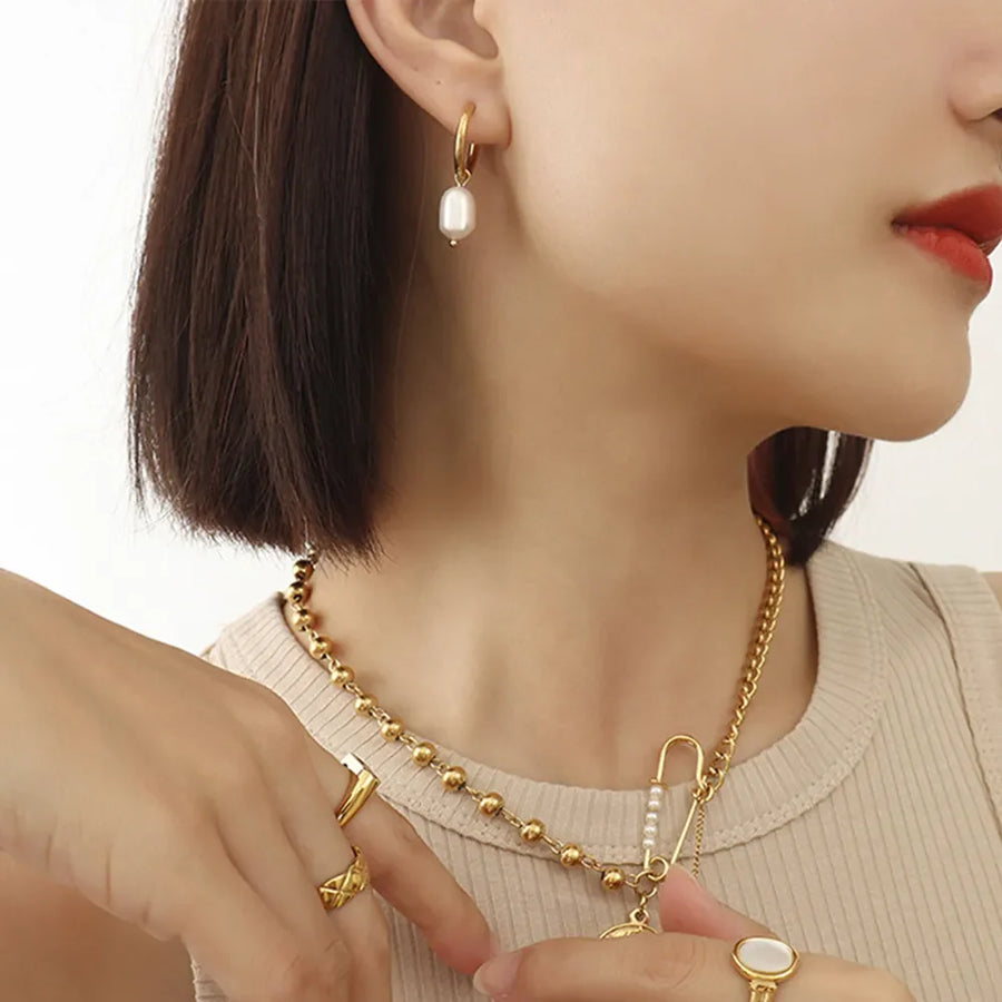Gold hoop earrings with lustrous pearl drop, styled with a gold beaded necklace.