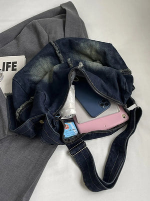 Dark wash denim crossbody bag with frayed edges and distressed details, open to show contents.