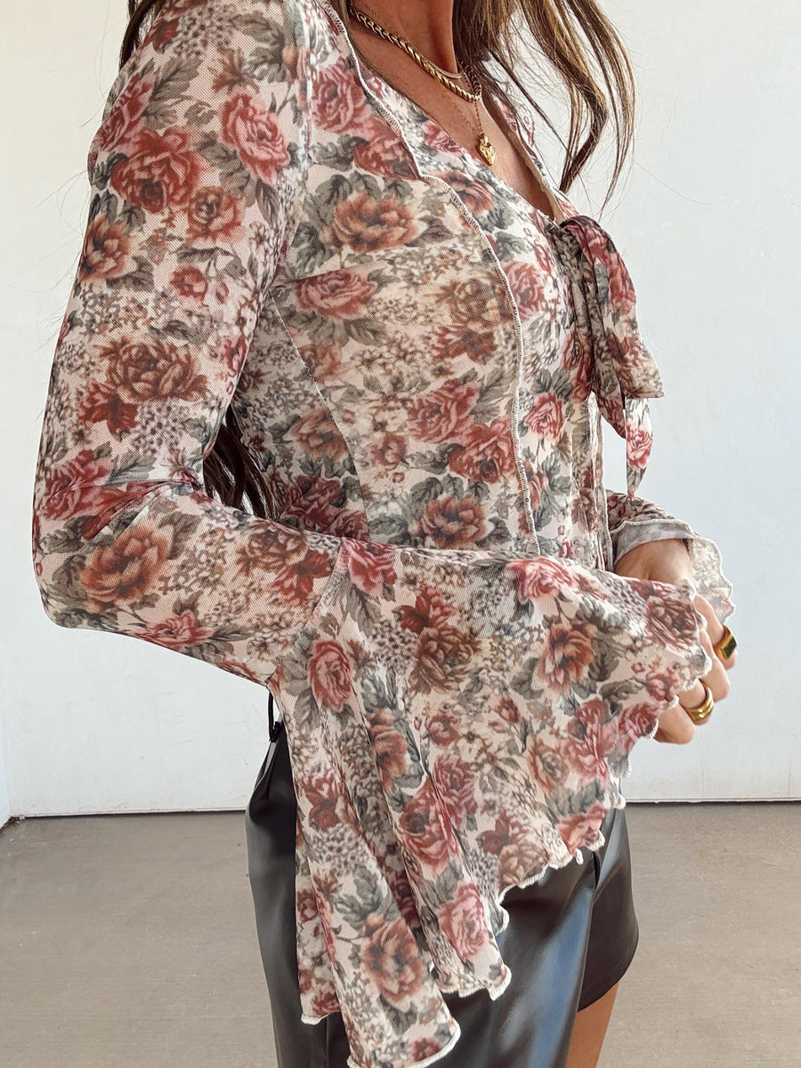 Charming floral mesh blouse with tied ruffle neckline and bell sleeves.