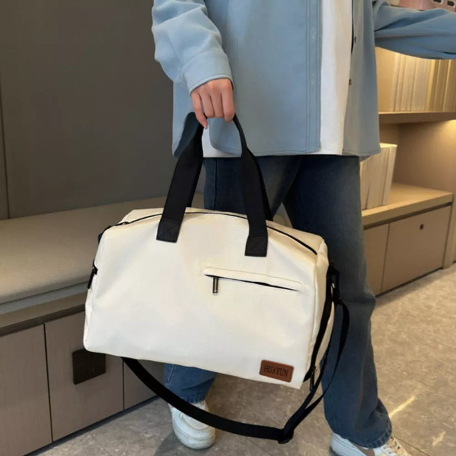 Creamy-white nylon travel duffel bag with black handles and adjustable strap, featuring a front zip pocket.