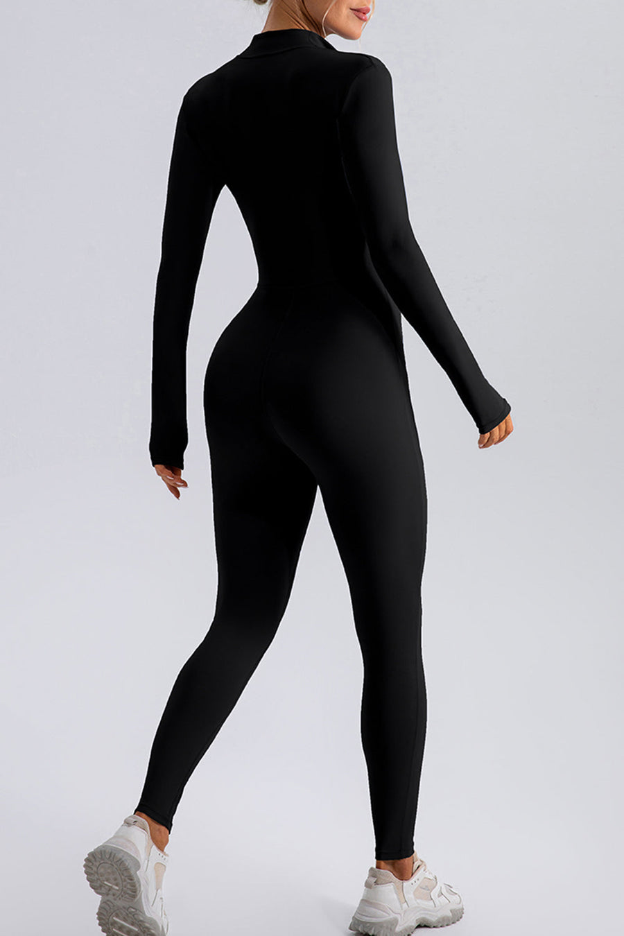 Black zip-front bodycon jumpsuit with long sleeves and thumbholes, worn with sneakers