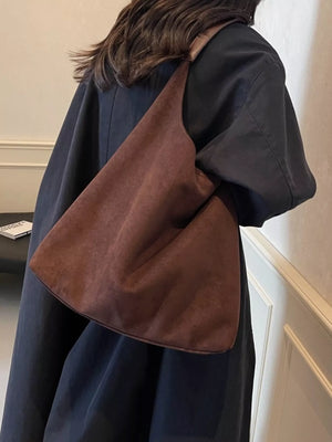 Brown suede hobo bag with leather strap detail worn over the shoulder.