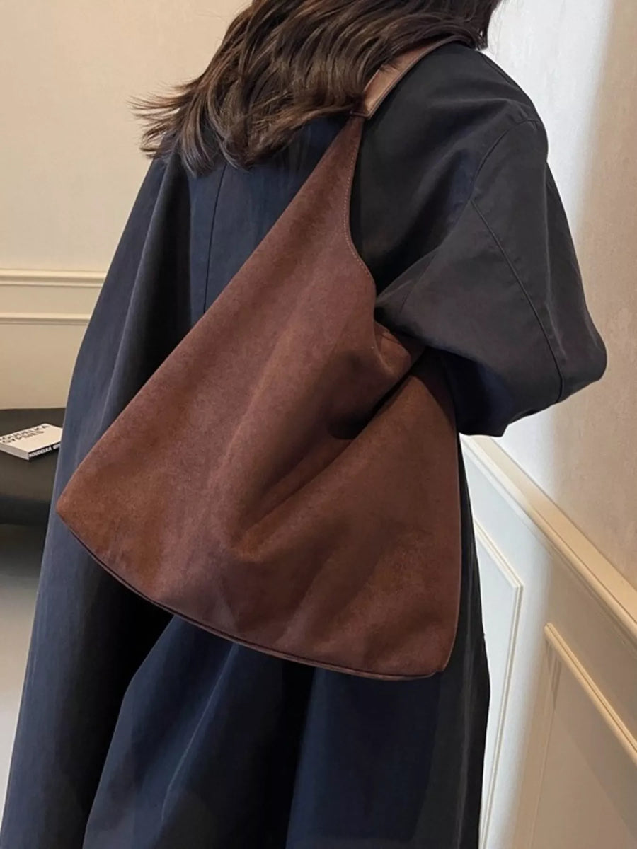 Brown suede hobo bag with leather strap detail worn over the shoulder.