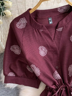 Burgundy paisley print jumpsuit with drawstring waist and short sleeves.