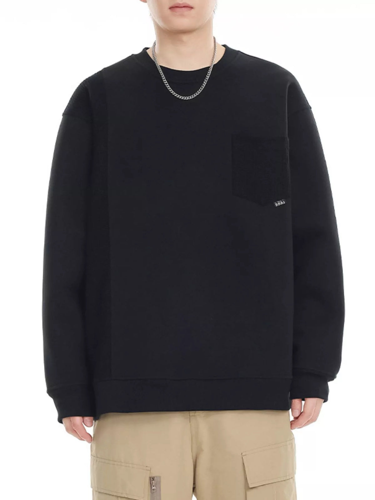 Black crewneck sweatshirt with chest pocket and subtle patchwork detail.