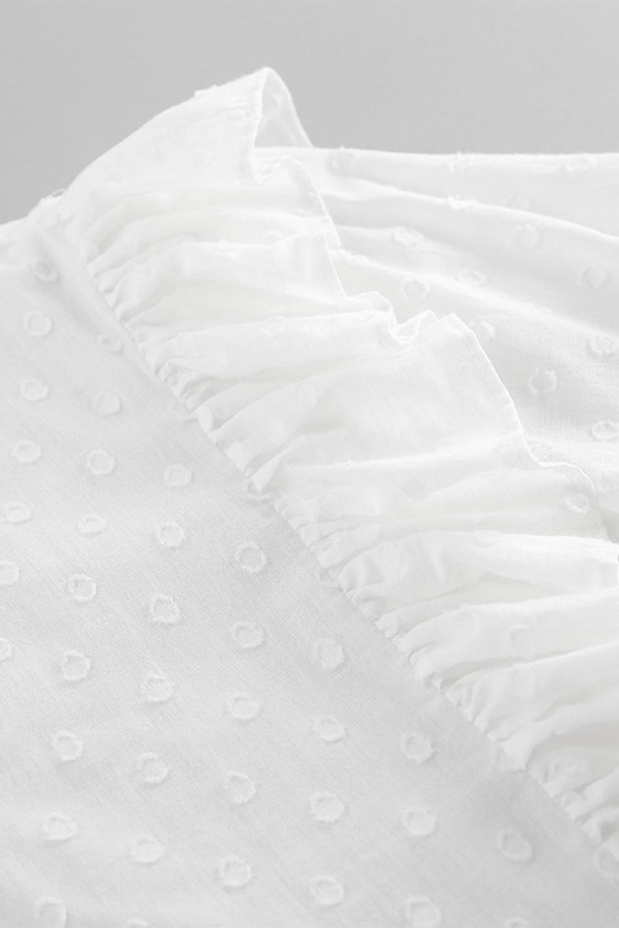 White textured shirt with ruffle trim and dot pattern detail