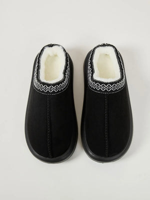 Black shearling house slippers with embroidered trim and white sherpa lining.