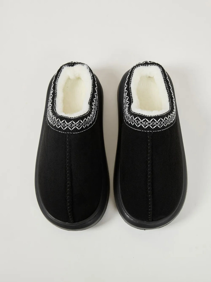Black shearling house slippers with embroidered trim and white sherpa lining.