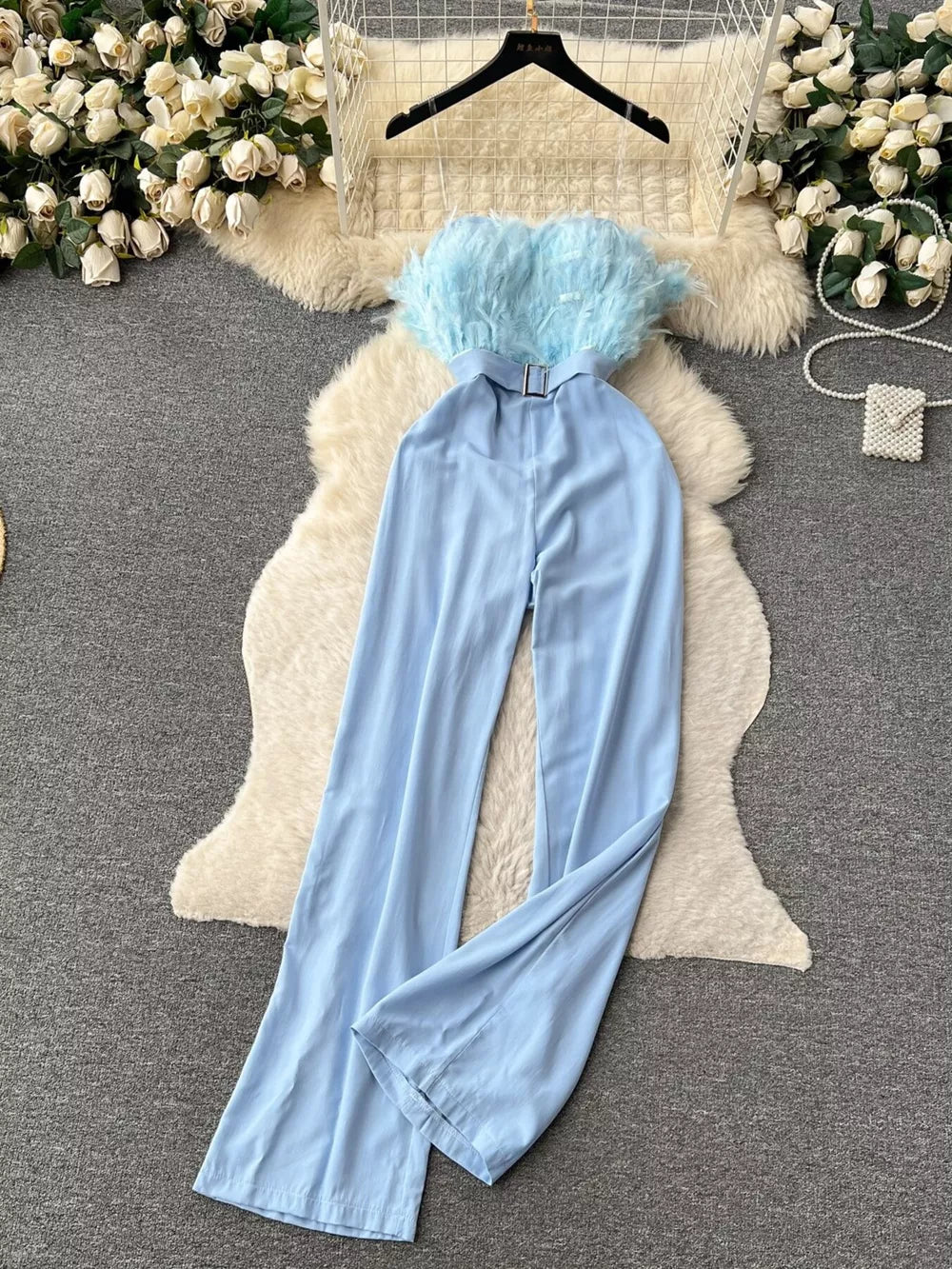 Blue strapless wide-leg jumpsuit with feather trim and belted waist.