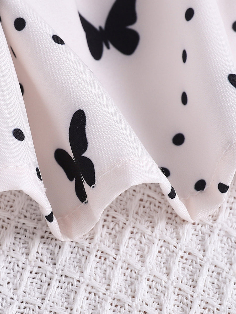 Baby dress with white fabric, black butterfly and polka dot print, and lace trim detail.
