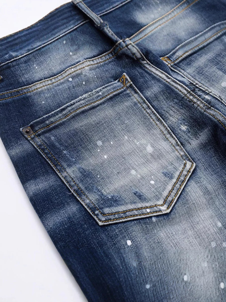 Men's dark blue distressed slim-fit jeans with paint splatter detail.