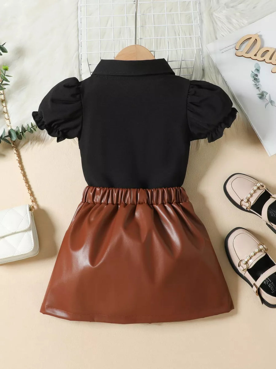 Black puff sleeve top with collared neckline and brown faux leather pleated skirt.
