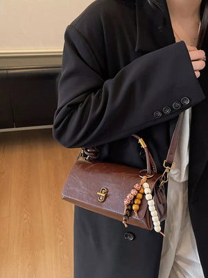 Brown leather crossbody bag with beaded charm and gold clasp