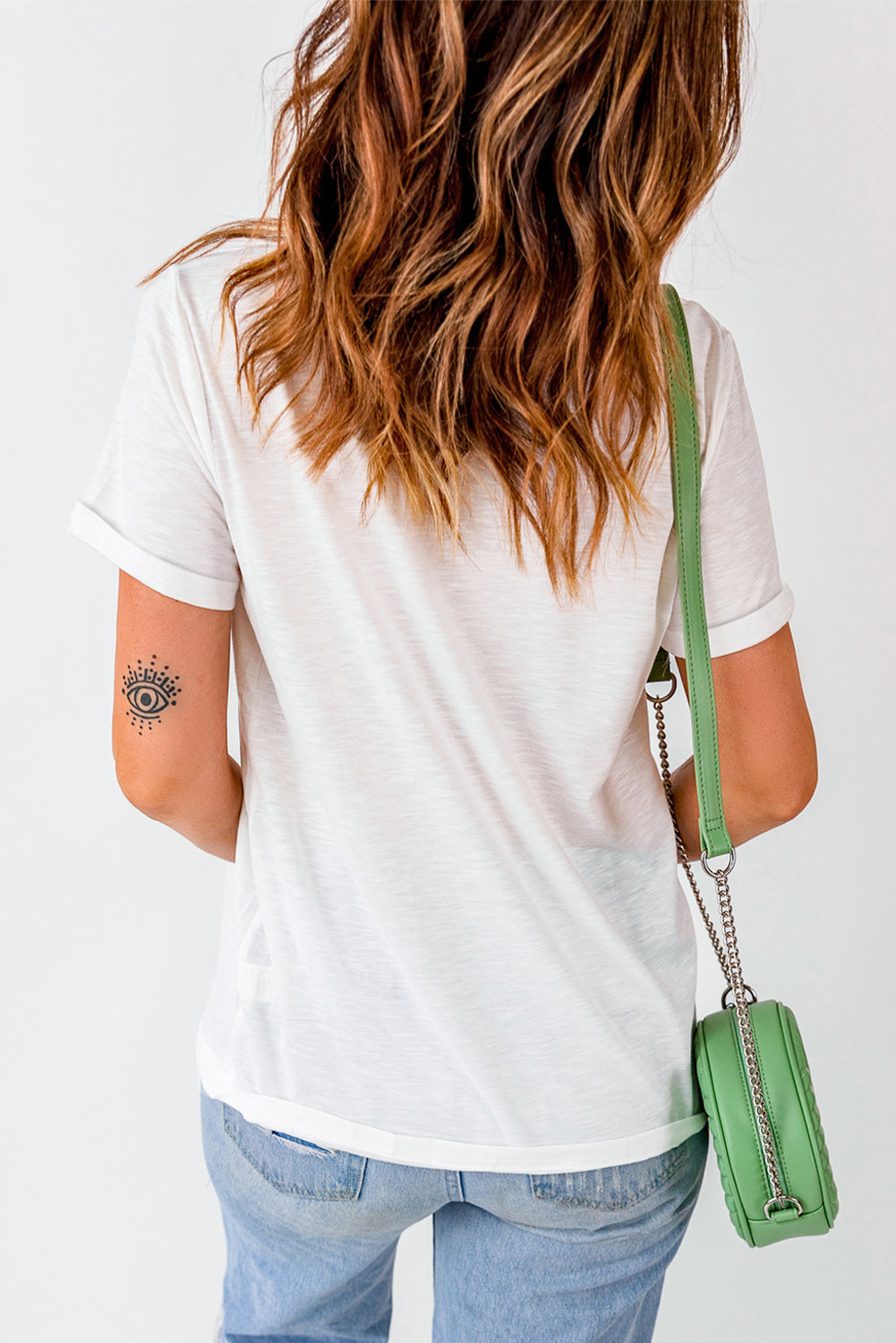 White graphic t-shirt with rolled sleeves and a subtle eye tattoo on the arm.