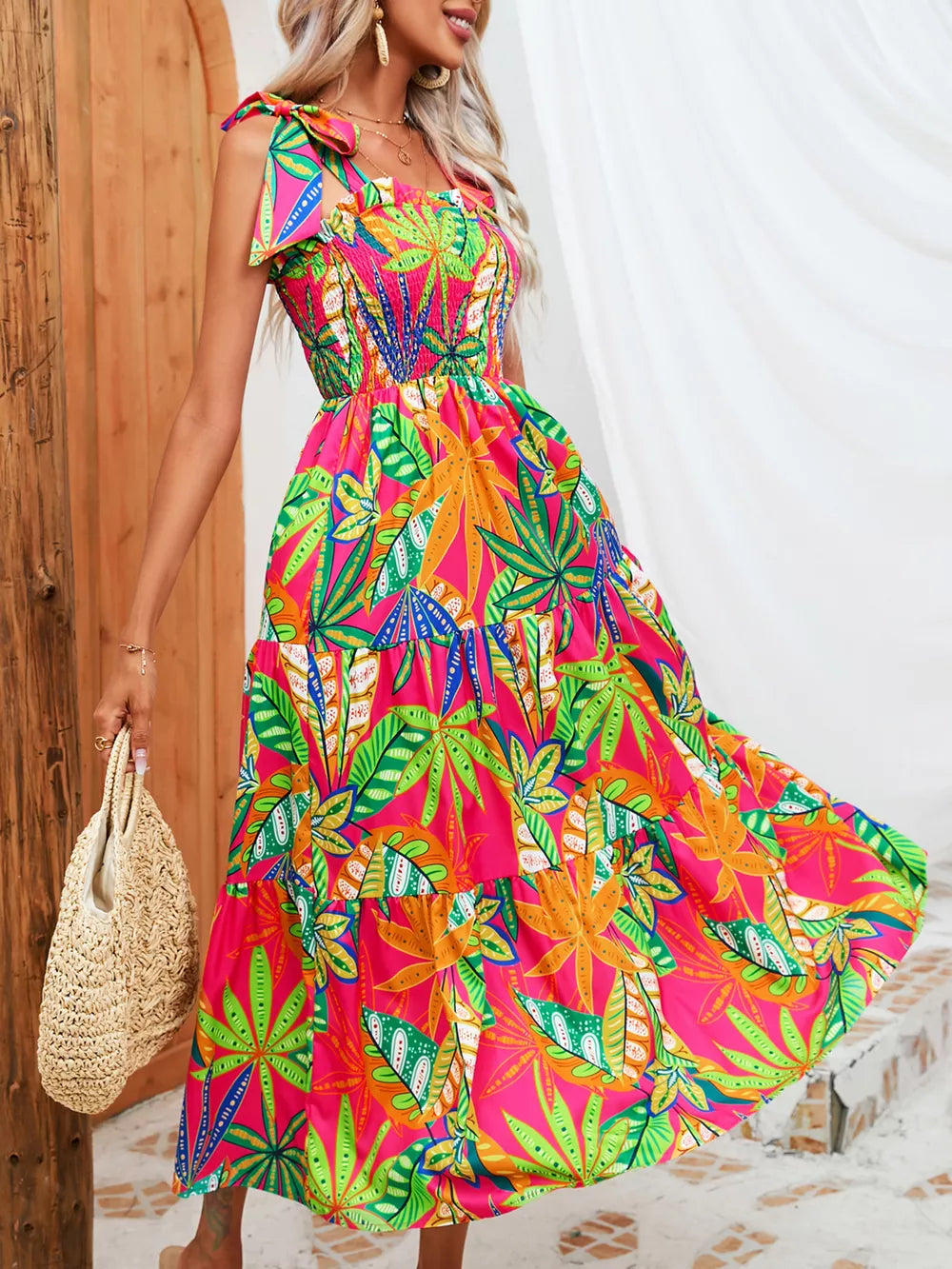 Tropical tie-strap smocked midi dress in pink with vibrant leaf print, tiered skirt.