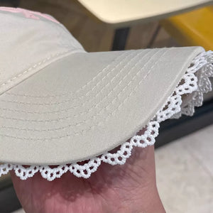 Beige baseball cap with white lace trim and embroidered pink bow detail.