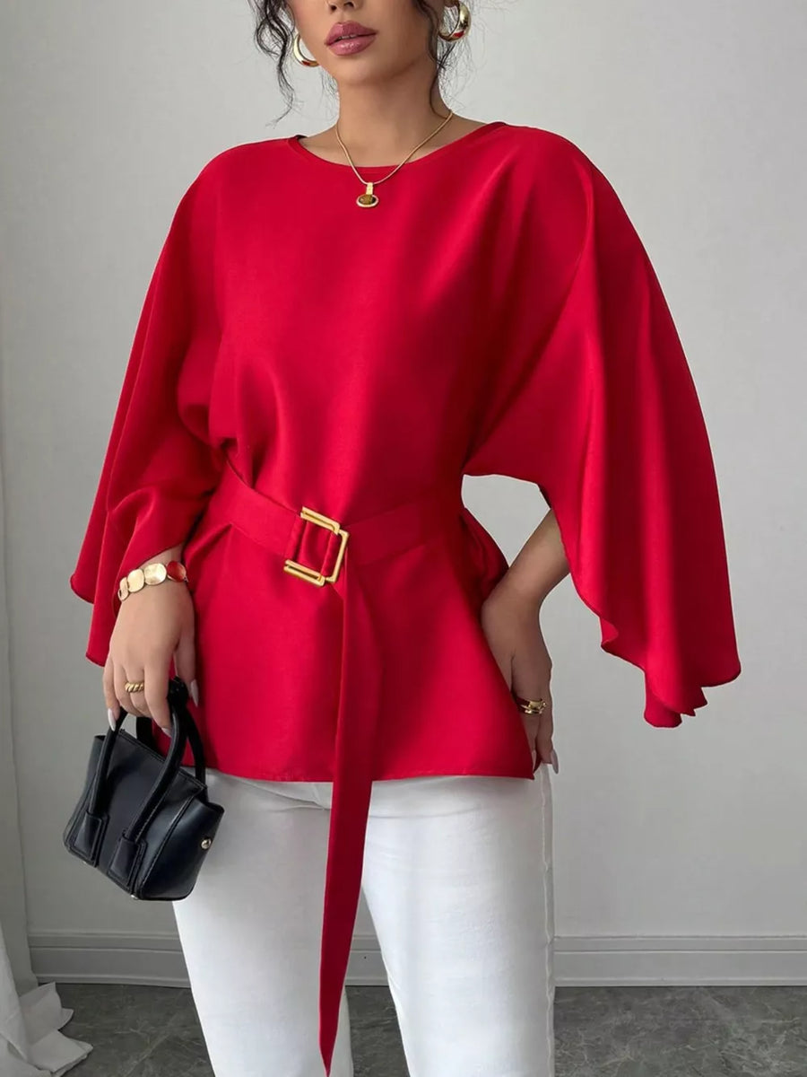 Red belted blouse with batwing sleeves and gold buckle detail, styled with white pants.