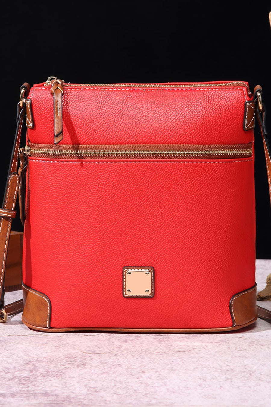 Red leather crossbody bag with brown trim and gold zippers.