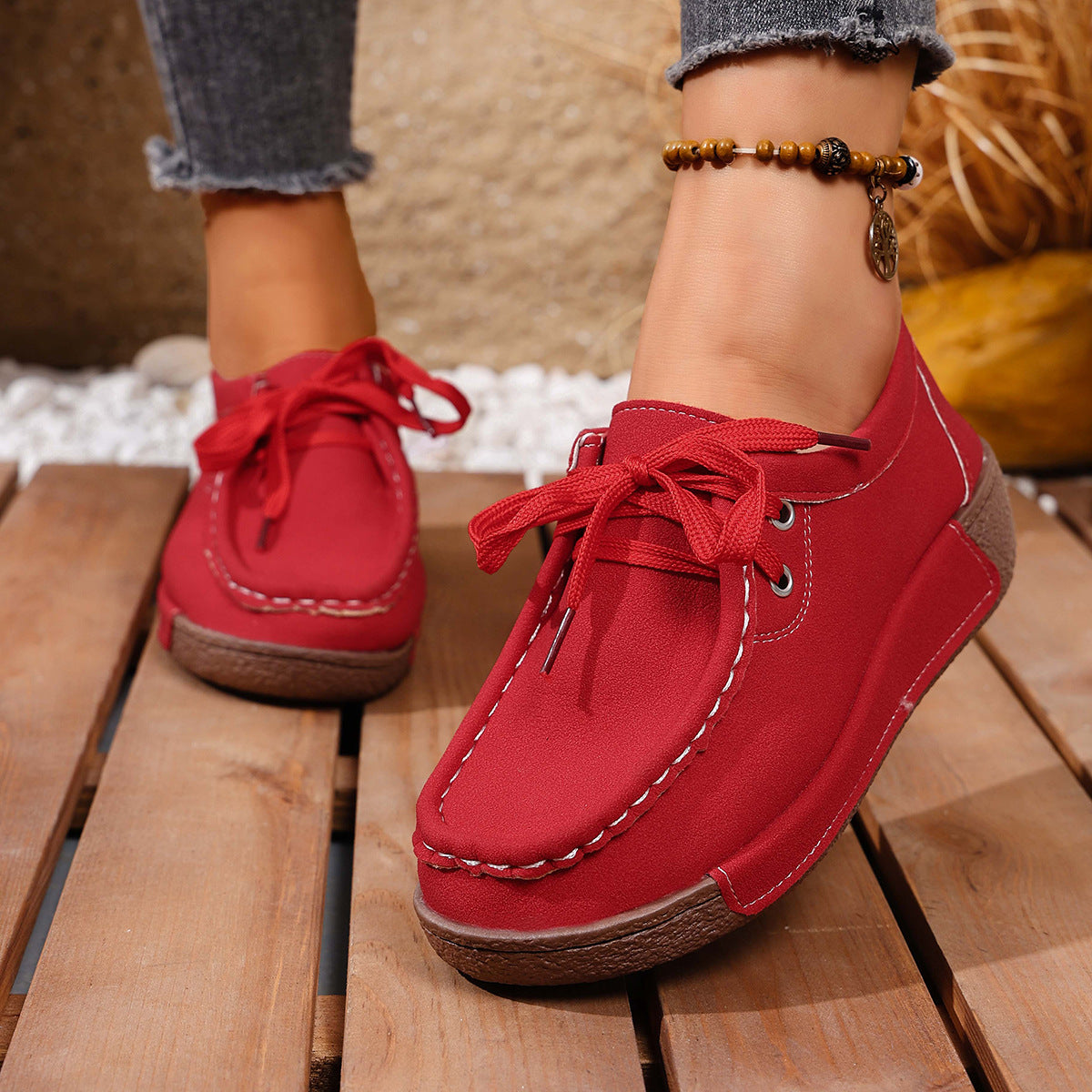 Red lace-up moccasin style sneakers with white stitching detail and a brown sole.