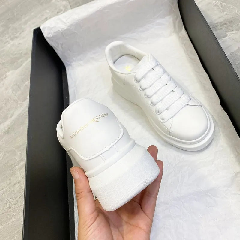 White platform sneakers with lace-up front and gold embossed heel detail.