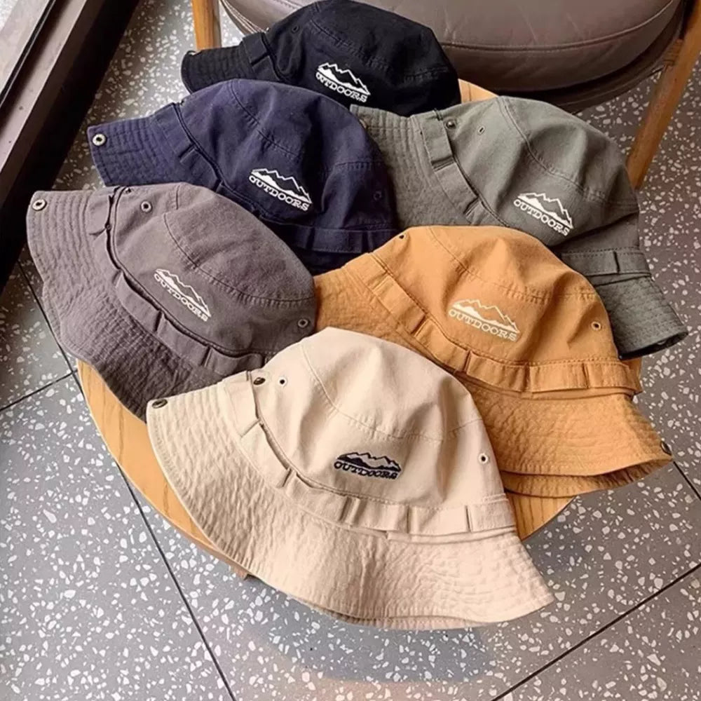 Bucket hats in black, navy, grey, olive, tan, and orange, each with a white mountain logo and "OUTDOORS" text.