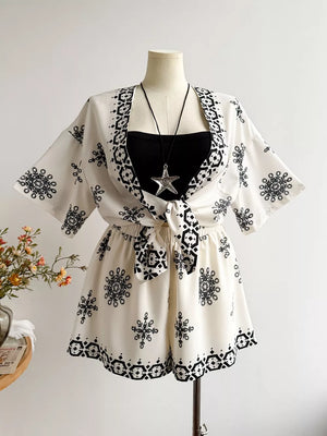White polyester two-piece set with black geometric and snowflake print, featuring a tie-front cardigan and shorts.