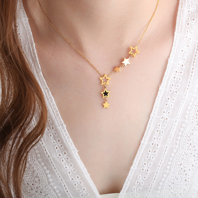 Gold celestial star necklace with cascading stars and a delicate chain, styled on a white lace top.