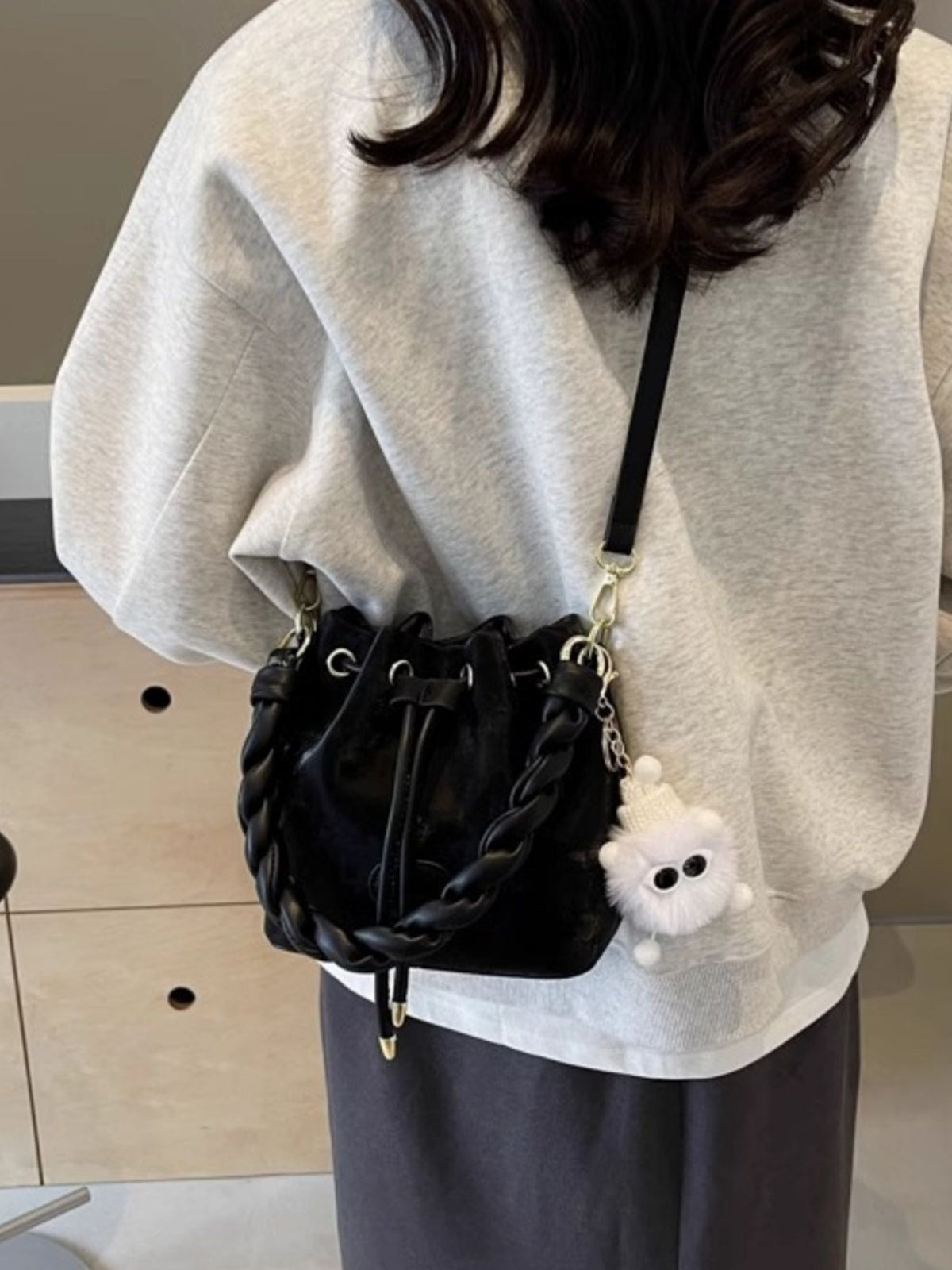 Black bucket bag with braided trim and chunky chain detail, worn crossbody.