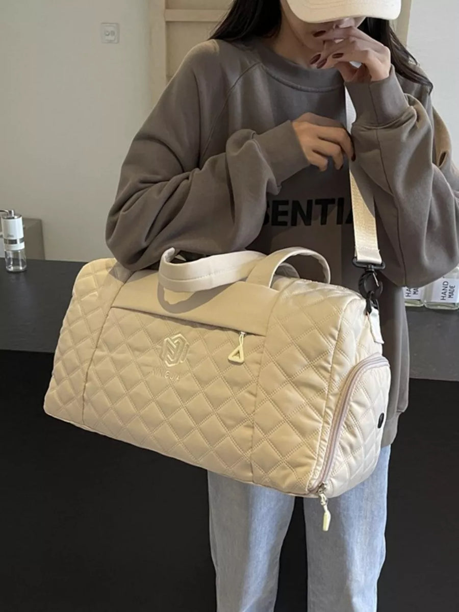 Diamond-stitched beige quilted duffel bag with adjustable strap and front logo detail.