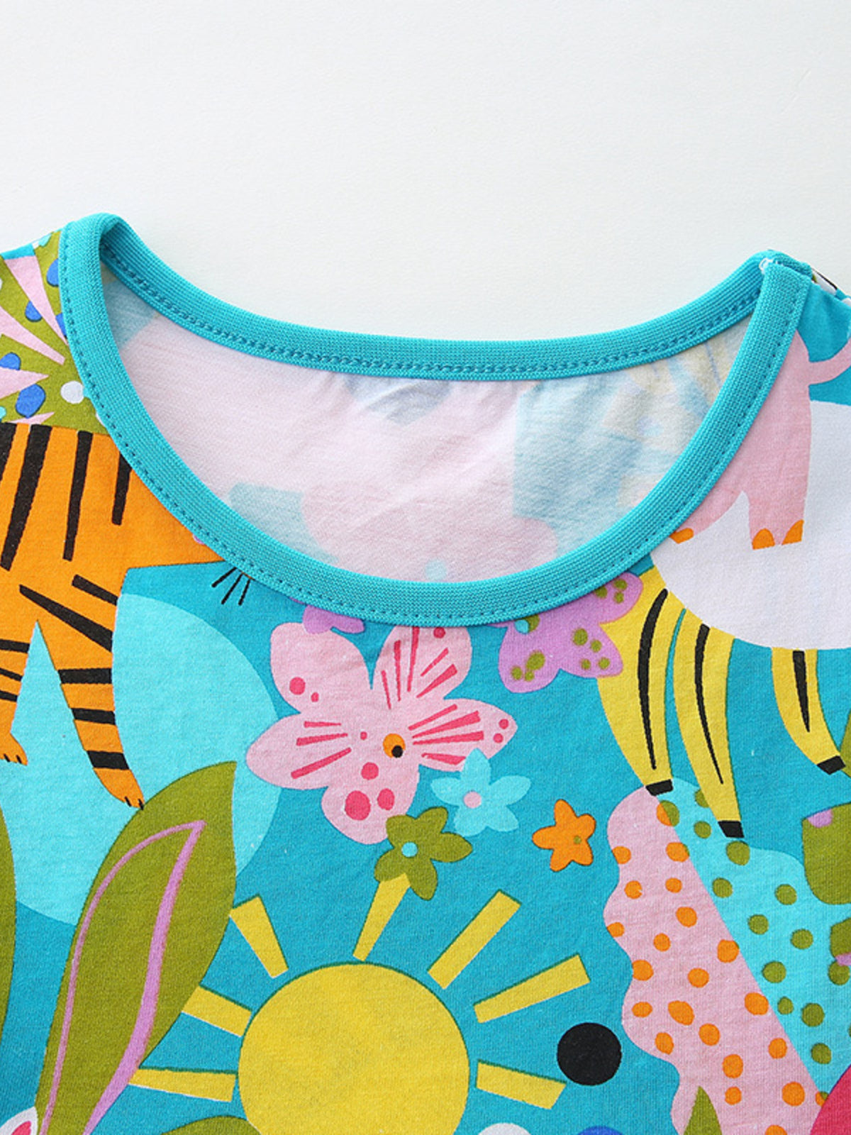 Toddler cotton dress with vibrant safari print, featuring animals and flowers, and a turquoise neckline.