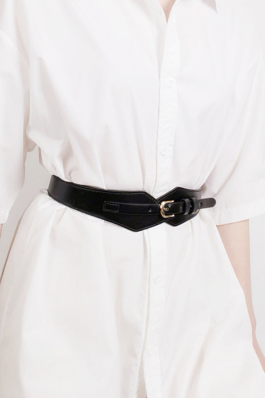 Black leather belt with geometric shape and gold buckle cinching a white shirt.
