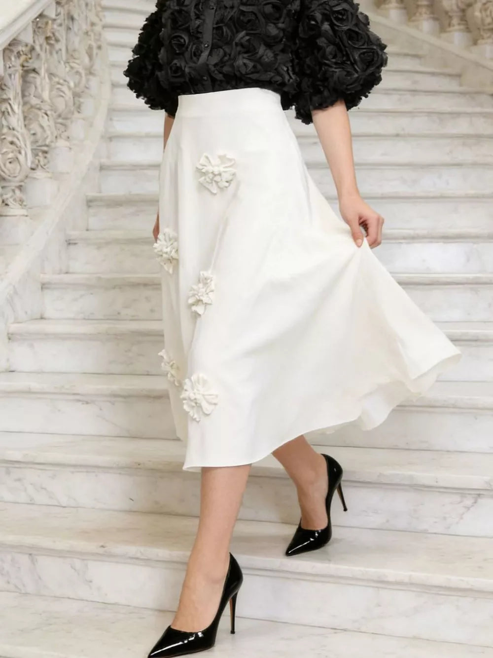White midi skirt with floral applique detail and black puff-sleeve top.