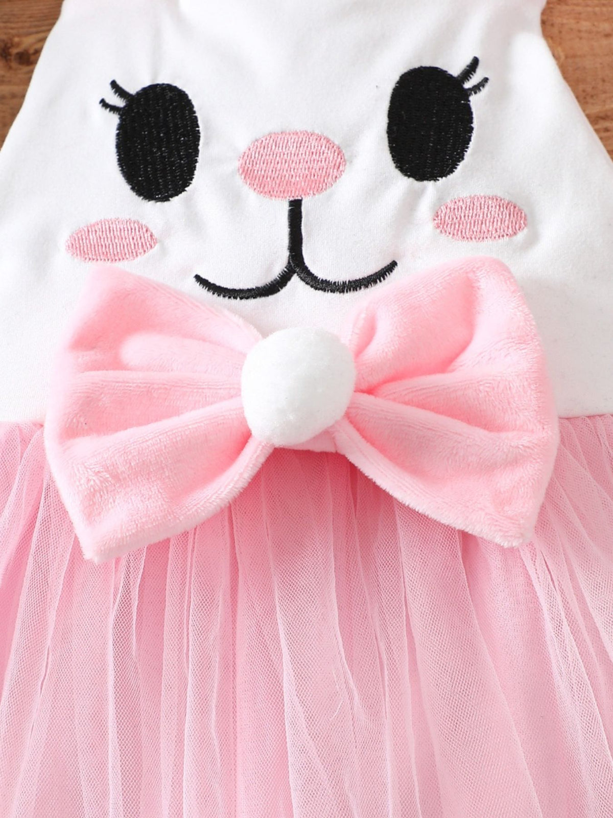 White baby one-piece with embroidered bunny face, pink bow, and pink tulle skirt.