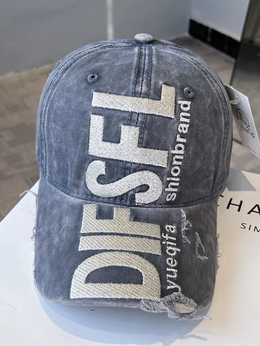 Distressed grey baseball cap with white embroidered text and frayed details.