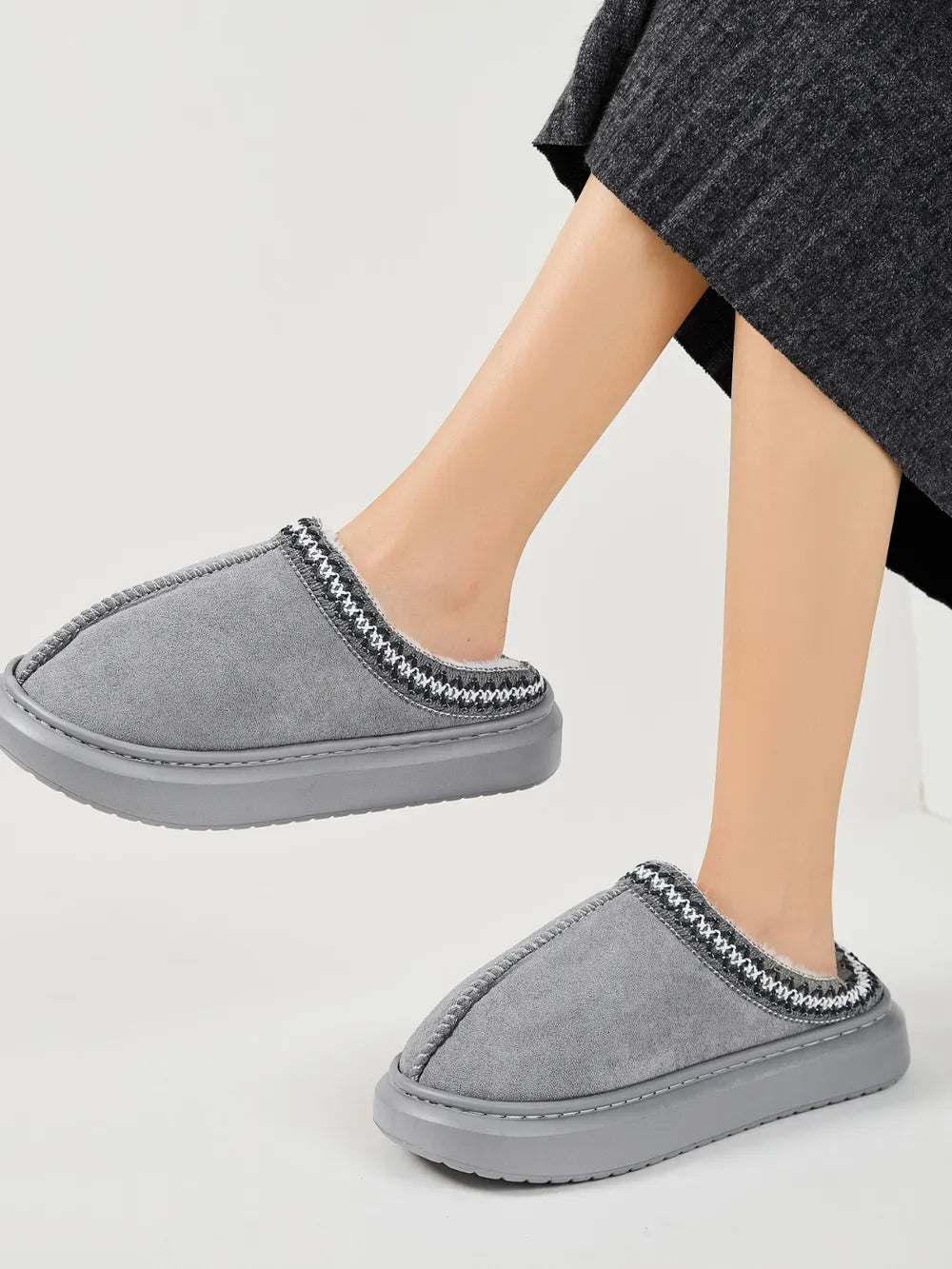 Gray shearling house slippers with embroidered trim and thick soles.