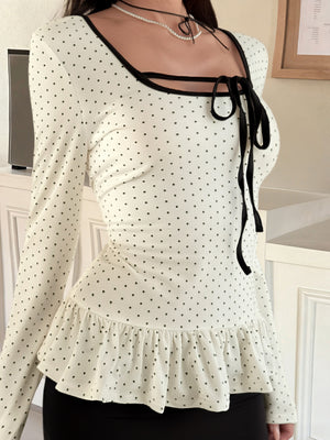 Ruffled polka dot long-sleeve t-shirt with black trim and tie-neck detail.