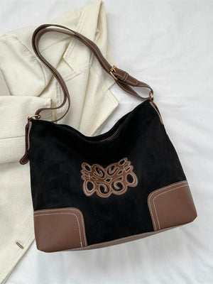 Black suede hobo bag with brown leather trim, contrast stitching, and appliqué detail.