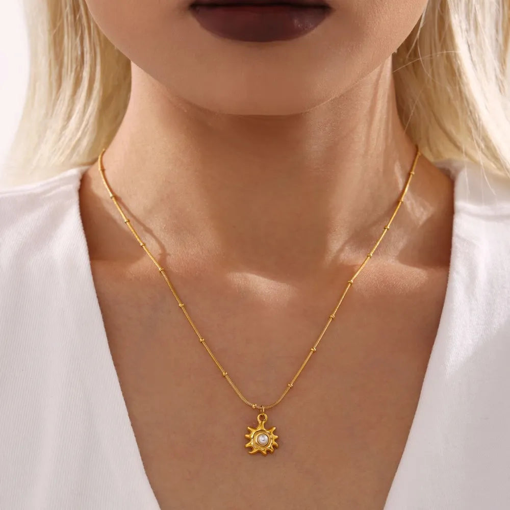 Gold sunburst pendant necklace with pearl detail on a beaded chain.