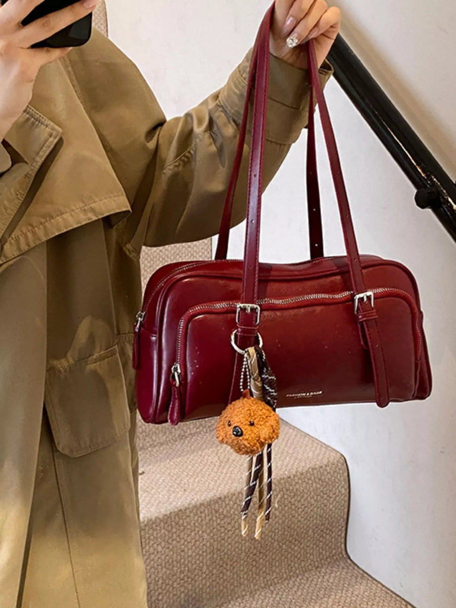 Deep red leather shoulder bag with zipper pockets and a dog charm.
