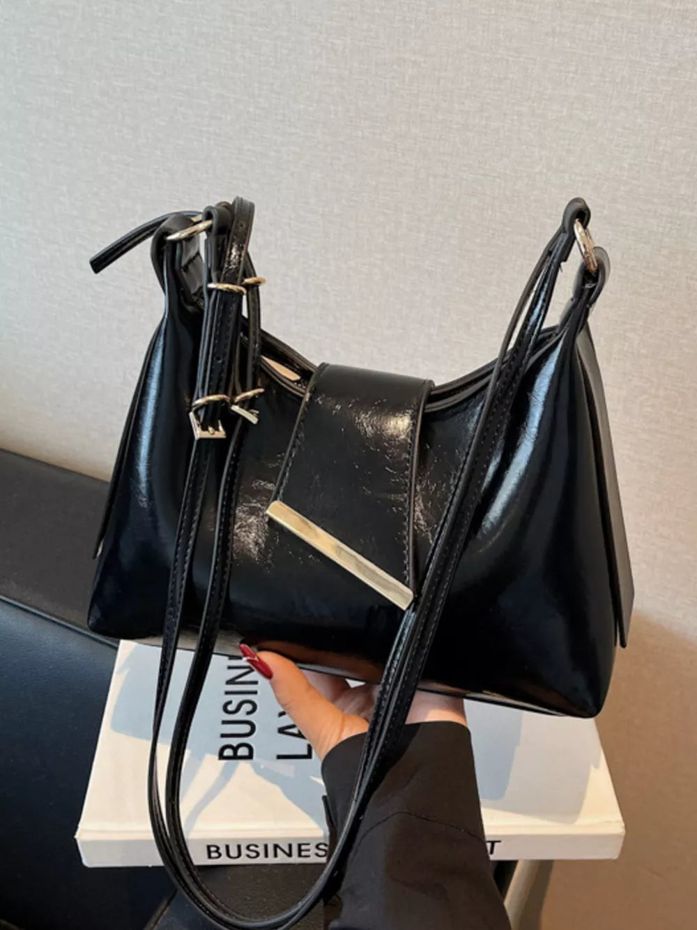 Black patent leather crossbody bag with adjustable straps and gold hardware detail.