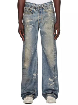 Distressed wide-leg jeans in medium wash denim with painterly splatters and fading.