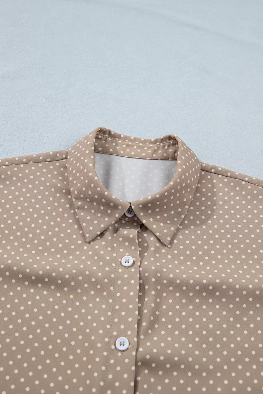 Chic polka dot button-up blouse with a collared neckline and cuffed sleeves.