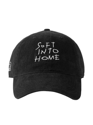 Black cotton baseball cap with white embroidered "SOFT INTO HOME" text and side graphic.
