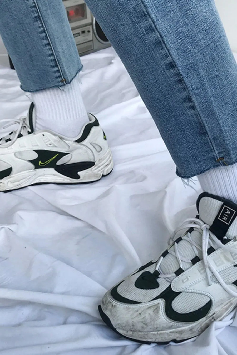 Medium wash denim jeans with raw hem and white socks, styled with sneakers.