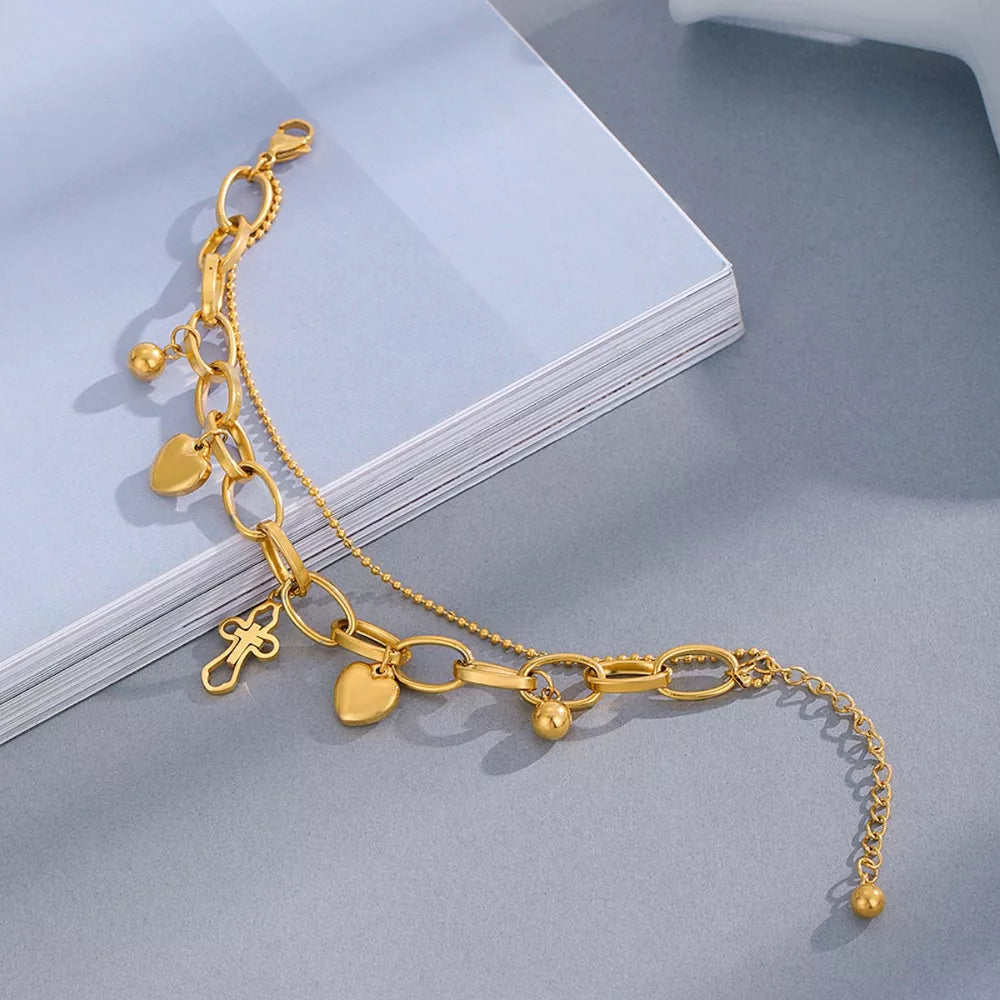 Gold charm bracelet with cross, heart, and bead charms on layered chains.